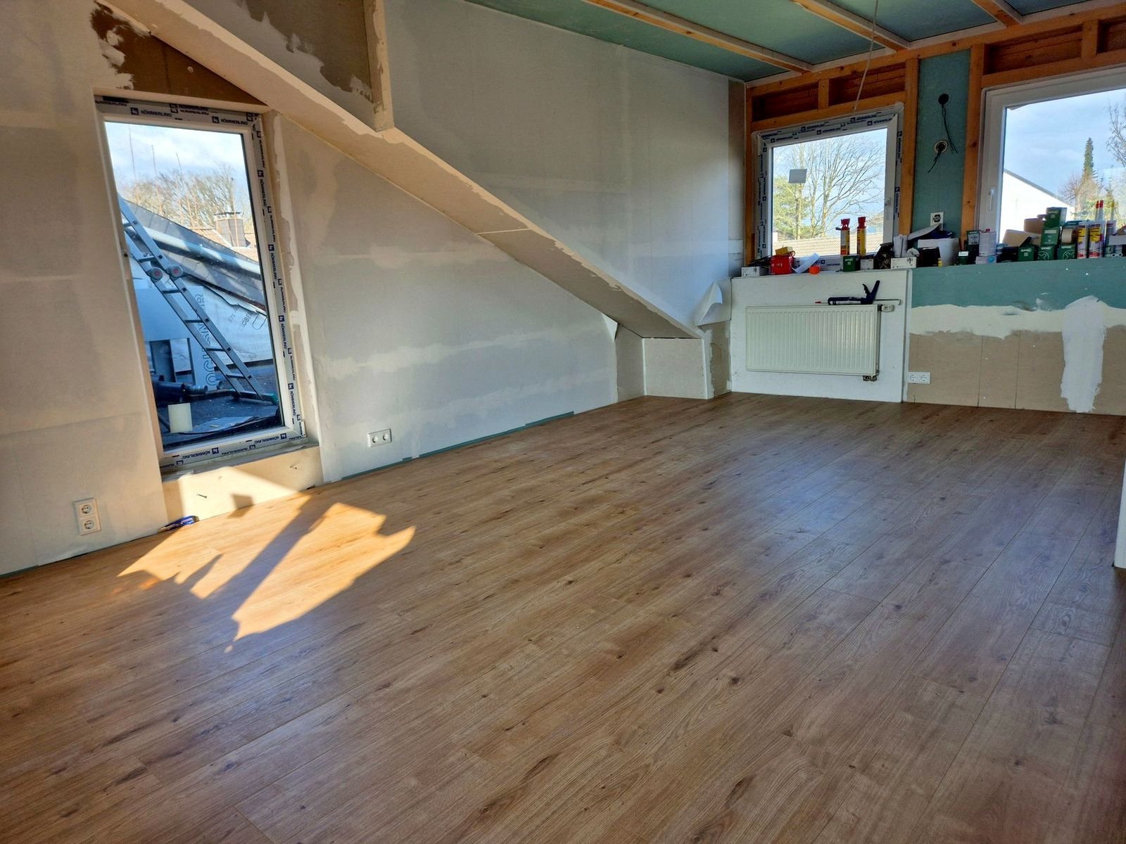 Dachgeschoss mit Boden in Holzoptik, Sonnenlicht fällt durch ein Dachfenster auf den Boden