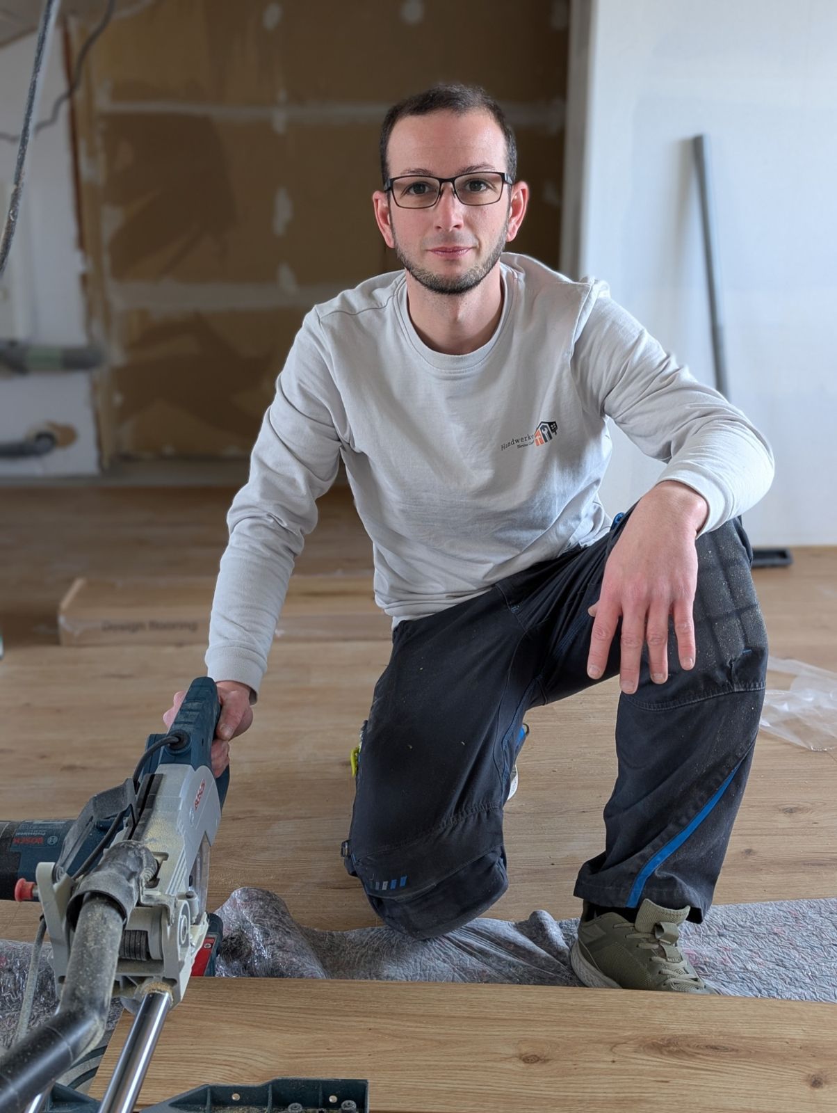 Marcel Blesius, Geschäftsführer, kniet mit einer Säge auf einem frisch verlegten Holzboden