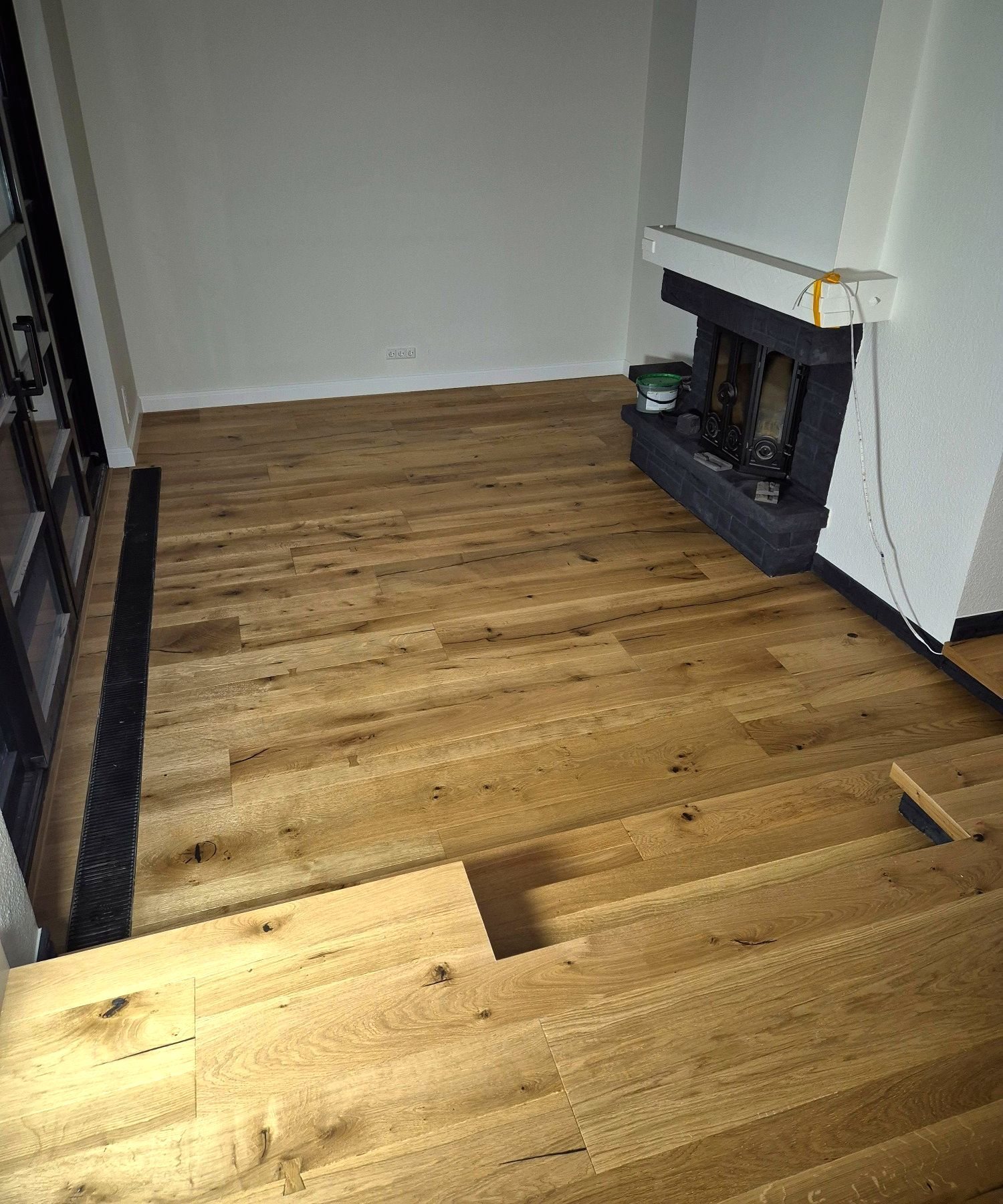 Eichendielen während der Verlegung in einem Wohnraum mit Kamin, im Vordergrund liegen noch einzelne Dielen lose